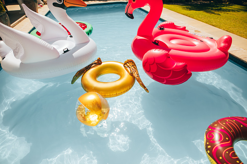 Group of colorful inflatable toys floating in a swimming pool on a summer day. Inflatable swan, flamingo, ring and ball in pool.