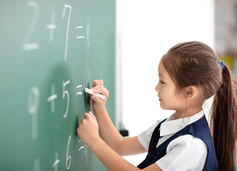 Happy schoolgirl writing answer on  blackboard