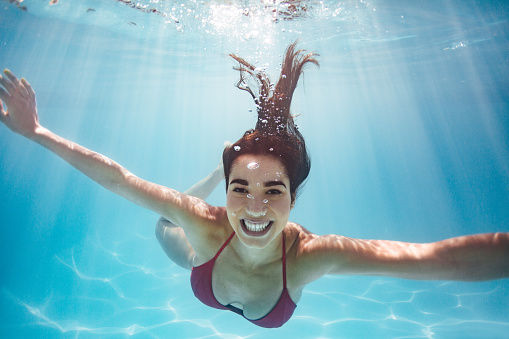 Underwater shot of a woman in swimming pool. Smiling female swimming underwater in holiday resort pool.