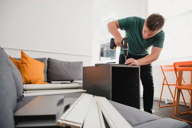 Young man putting up flat pack furniture in his new home.