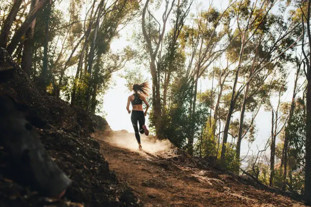 Rear view of woman trail running on a mountain path. Runner working out in beautiful nature.