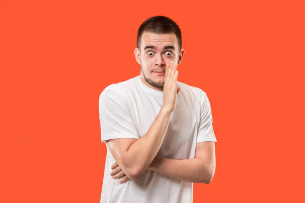 istock The young man whispering a secret behind her hand over orange background 1005961342