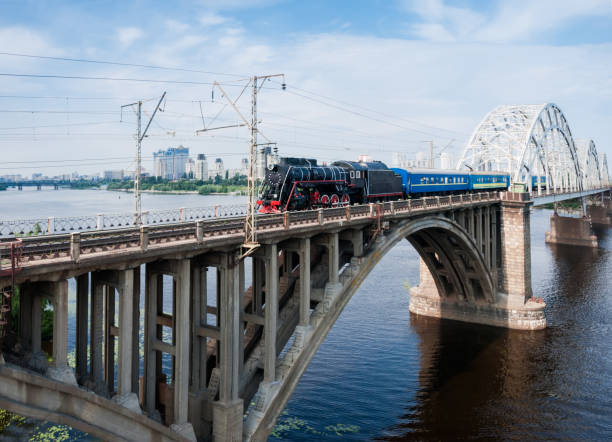 istock Steam locomotive with passenger train in motion on bridge 1005965880