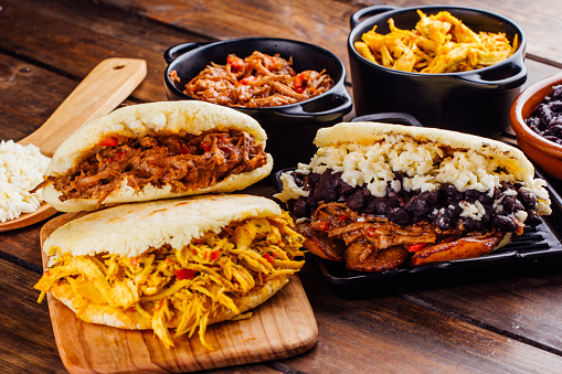 Latin American breakfast, specifically in countries such as Venezuela and Colombia, Arepas with several ingredients to fill like chicken, meat, black beans, fried plantain. All on a wooden rustic table