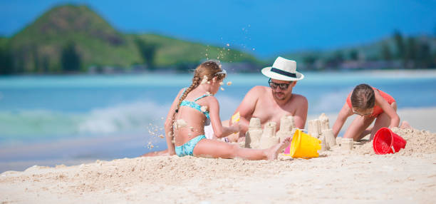 istock Father and two girls playing with sand on tropical beach 1005979234