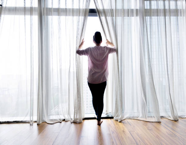 istock Woman opening curtains and looking out 1006001876