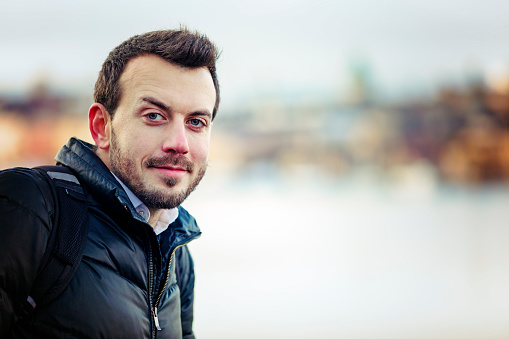 A young man with a beard and a bun sits on the rocks by the river, copy space.