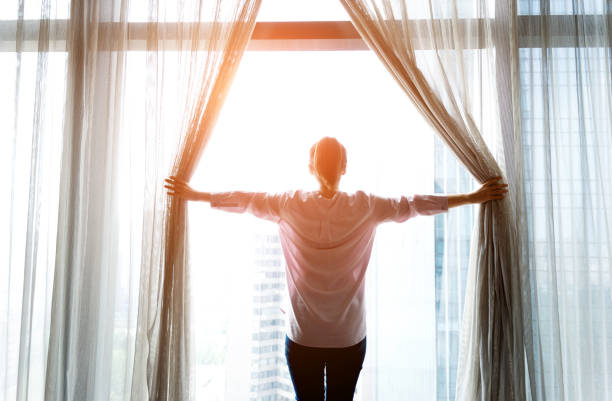 istock Woman opening curtains and looking out 1006001990