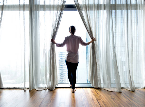 istock Woman opening curtains and looking out 1006002066