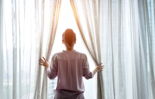 istock Woman opening curtains and looking out 1006002124