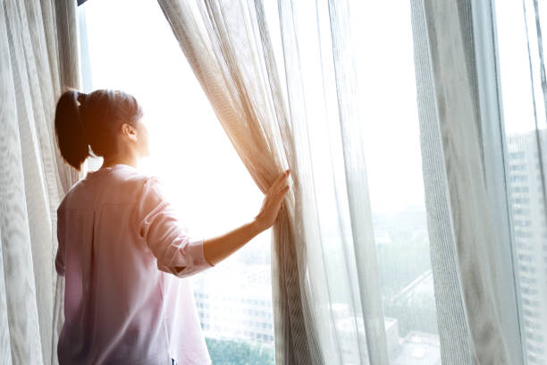 istock Woman opening curtains and looking out 1006002482