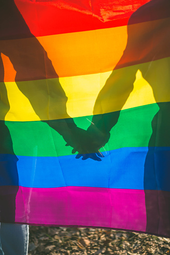 people, homosexuality, , gay and love concept - close up of happy male gay couple hands over rainbow flag