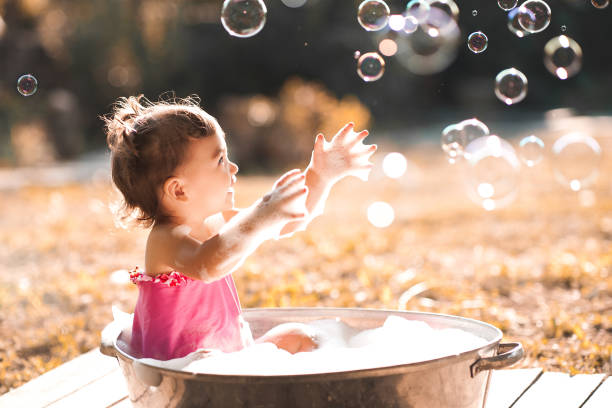 Baby girl washing outdoors Laughing baby girl 1 year old playing with soap bubbles outdoors. girls bath stock pictures, royalty-free photos & images