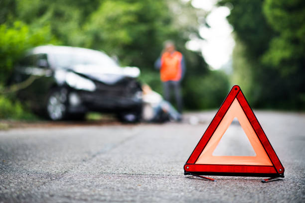 A close up of a red emergency triangle on the road in front of a car after an accident. A close up of a red emergency triangle on the road in front of a damaged car and unrecognizable people. A car accident concept. Copy space. car accident stock pictures, royalty-free photos & images