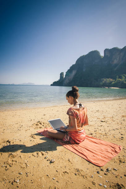 istock Woman freelance on laptop computer at tropical, exotic beach 1006049014