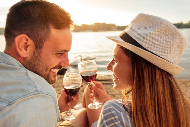 szczęśliwa młoda para robi toast z czerwonym winem. ciesząc się piknik na plaży - swimming animal beach casual loving zdjęcia i obrazy z banku zdjęć