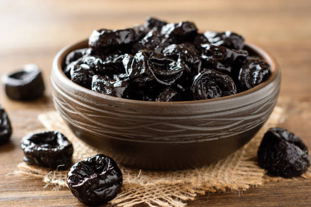 Prunes in ceramic bowl on rustic wooden table. Dried plums.