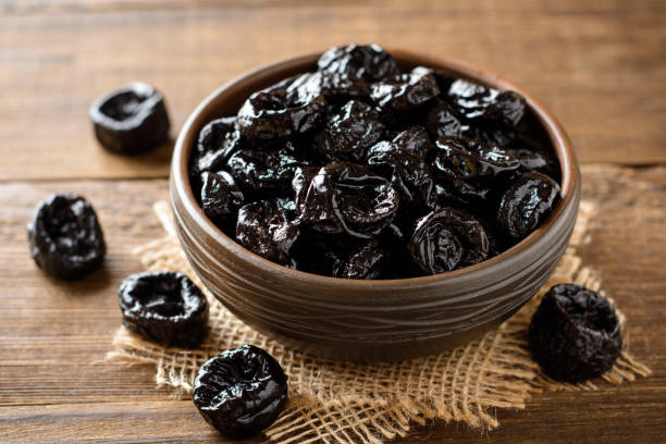 istock Prunes in ceramic bowl on rustic wooden table. Dried plums. 1006057722