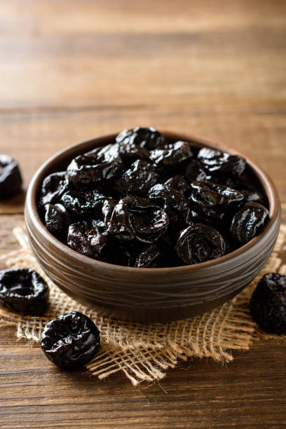 istock Prunes in ceramic bowl on rustic wooden table. Dried plums. 1006057820