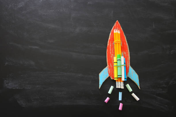 istock Back to school concept. Top view image of handmade cardboard rocket and clouds with pencils over classroom blackboard background 1006058604
