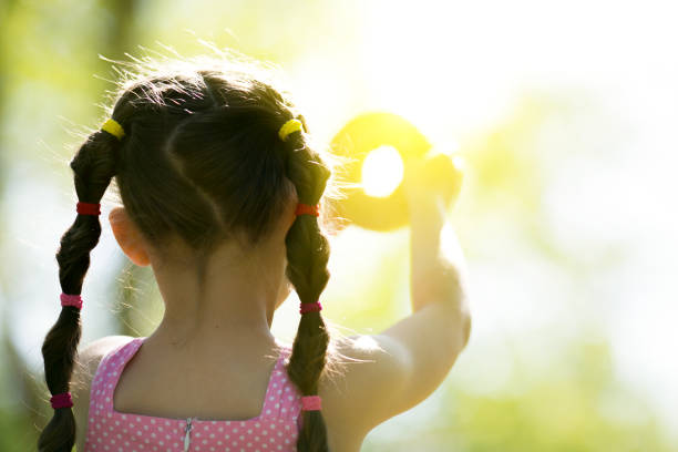 The girl through the hole in the bread looks at the sun in the sky.