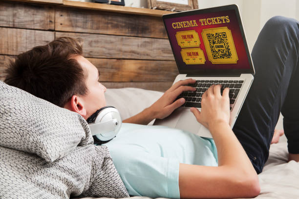 istock Man buying on line cinema tickets on the internet with a laptop computer, while lying down on the bed at home. 1006074696