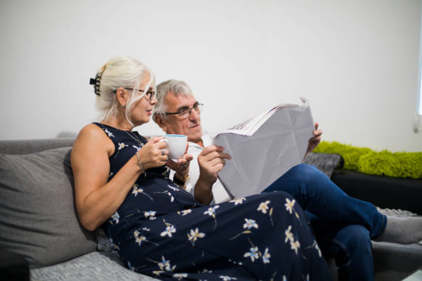 istock Senior Couple Relaxing On Sofa At Home Reading Newspaper 1006081764