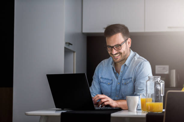 istock Handsome man using laptop computer at home, drinking juice and coffee in the morning 1006088674