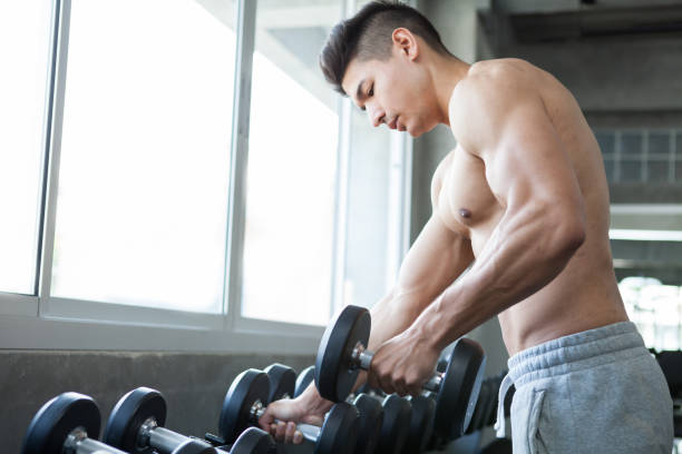istock Muscular bodybuilder guy doing exercises standing select with weight lifting dumbbells in gym . sport young fitness man training . focus chest 1006098210