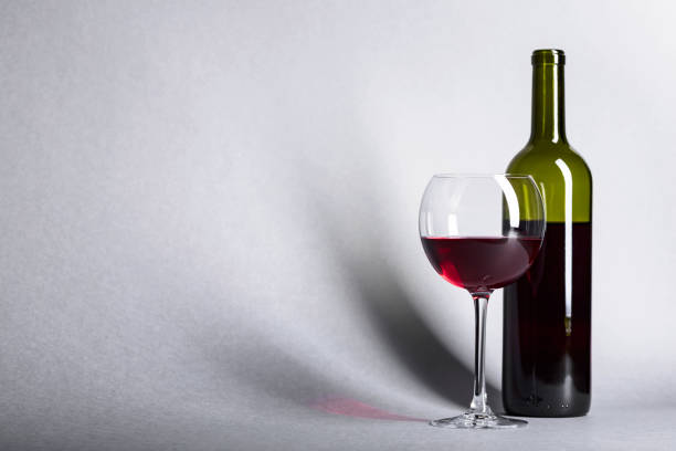 A glass and bottle of red wine and red grapes with reflaction on dark background