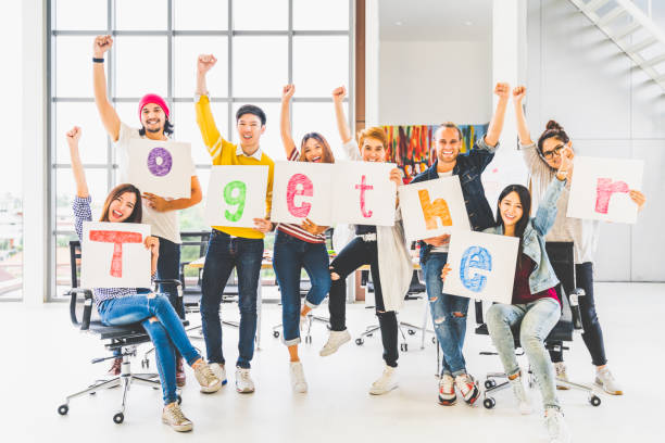 Multiethnic diverse group of office coworkers or creative team cheering and celebrating, holding letter banner papers written together word. Colleague partner teamwork, team building, empowerment, or friendship togetherness concept