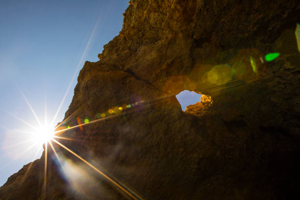 The sun peeking over the rugged cliff edge of the stunning Benagil Caves, located along the Algarve coast in Portugal.