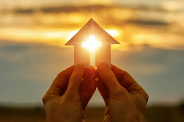 Photo of Hands with paper prayer house in the hands .