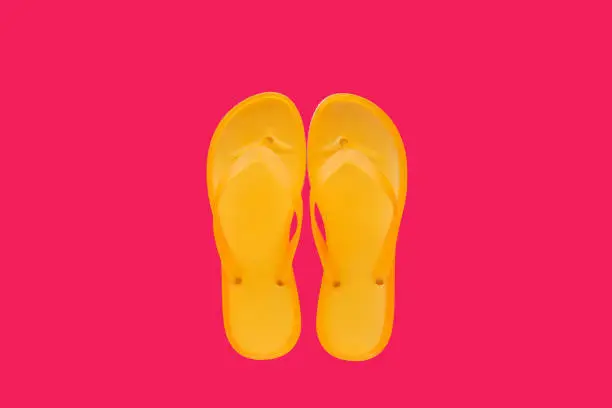 Photo of Yellow beach flip flops on neon pink background