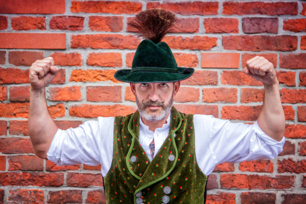 handsome bavarian man flexing his muscles handsome bavarian man flexing his muscles in front of brick wall Lederhosen stock pictures, royalty-free photos & images