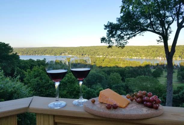 2 Filled Red Wine Glasses with Compliment of Cheese and Grapes in a Rustic, Water View Background, Nearing Dusk stock photo