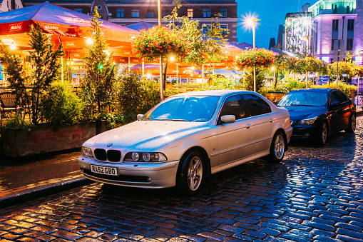 Riga, Latvia - July 3, 2016: Sedan Car BMW 5 Series E39 Parking Near Street Cafe In Evening Or Night Illumination In Old Town On Kalku Street