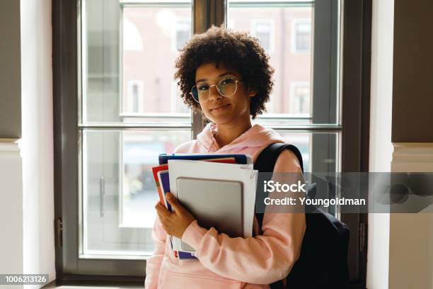 Beautiful Young Woman With Books And Digital Tablet Standing At Window In Campus Stock Photo - Download Image Now