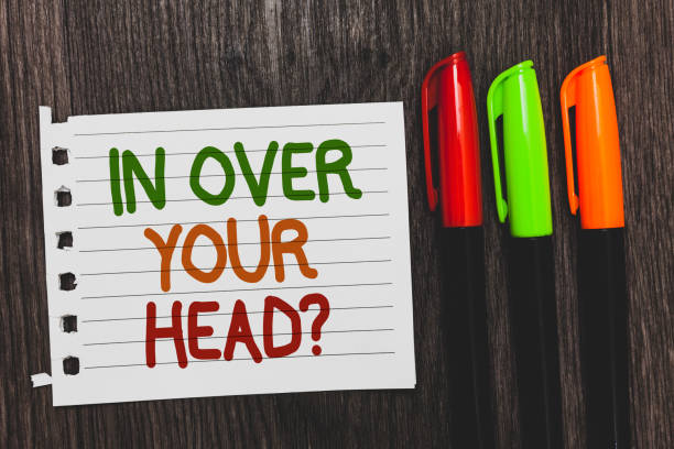 istock Handwriting text In Over Your Head question. Concept meaning To be involved in a difficult situation problem Colorful words with white page red green orange pen on blackish wooden desk. 1006216990