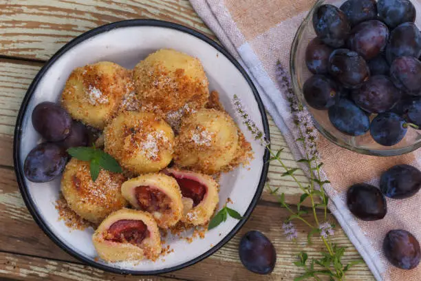 Sweet plum dumplings in metal bowl on wooden table. Homemade dessert with dough and plums.