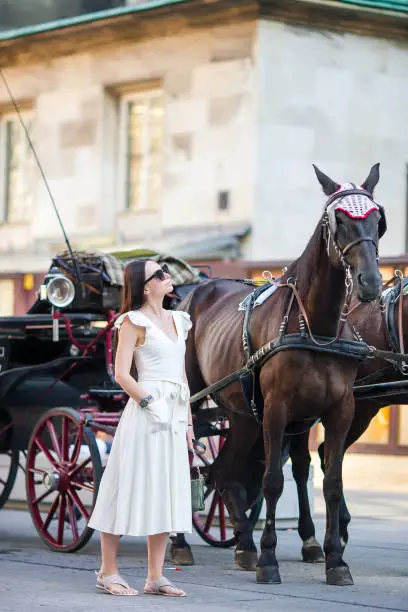 Tourist woman enjoying a stroll through Vienna and looking at the beautiful horses in the carriage. Beautiful girl in Europe