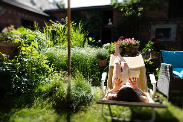 A young woman is lying in a cot reading a book in summer