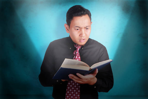 Portrait of young businessman holding and reading a book, amazed expression, source of knowledge concept, lighting the dark