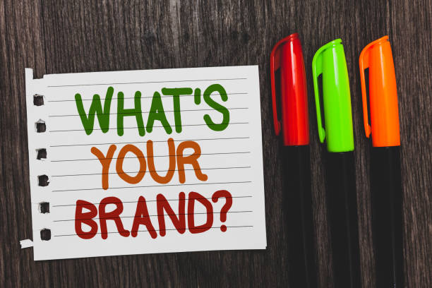 istock Handwriting text What s is Your Brand question. Concept meaning Define Individual trademark Identify Company Colorful words with white page red green orange pen on blackish wooden desk. 1006235406