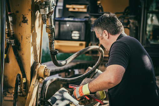 Construction worker repairing a piece of hydraulic heavy machinery.