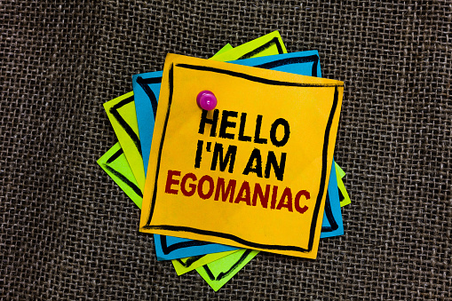 Text sign showing Hello I am An Egomaniac. Conceptual photo Selfish Egocentric Narcissist Self-centered Ego Black bordered different color sticky note stick together with pin on jute sack