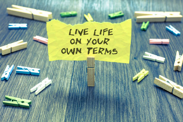 istock Handwriting text Live Life On Your Own Terms. Concept meaning Give yourself guidelines for a good living Paperclip hold written torn page many clips laid on bluish wooden floor. 1006247292