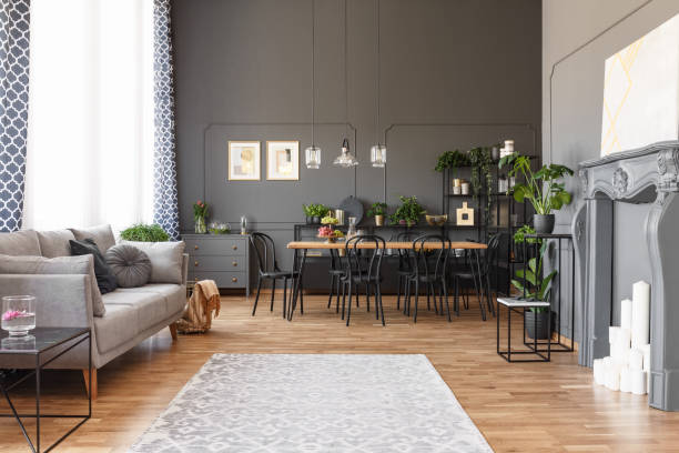 istock Open space apartment interior with gray sofa next to the window, dining table with black chairs and molding on the walls. Real photo 1006294988