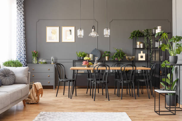 istock Open space apartment interior with black chairs at a wooden table in the dining area and metal racks with plants against dark wall with molding. Real photo 1006294992