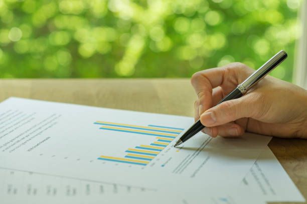 business, investment or financial report review, hand holding pen reviewing bar graph information data print on paper with green bokeh in the background - green report business bar graph imagens e fotografias de stock